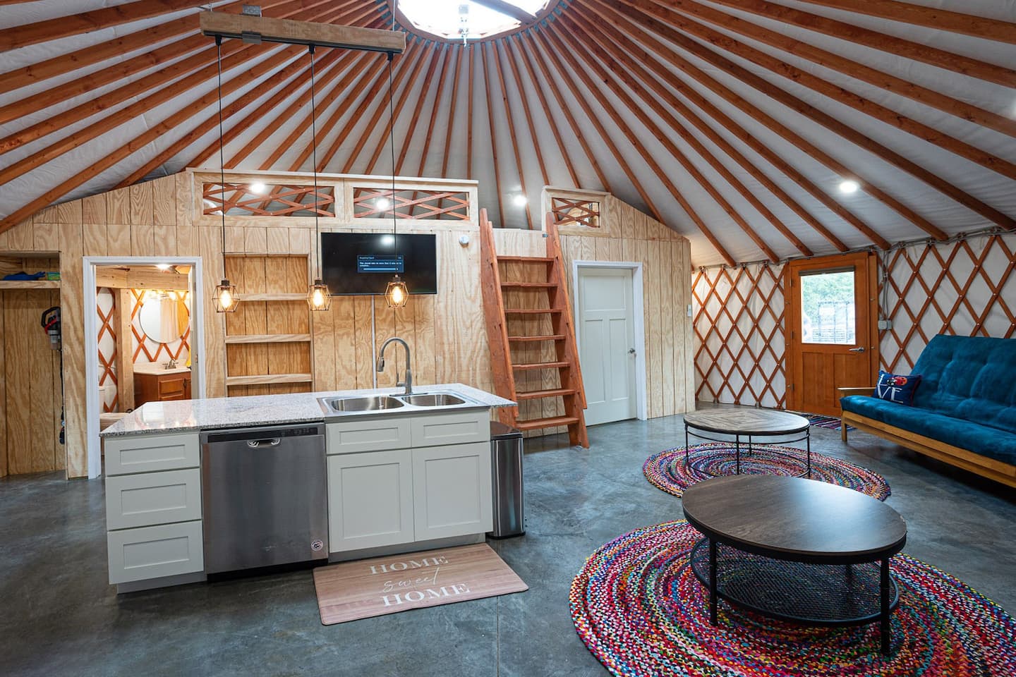 Yurt interior with full residential kitchen, wood cabinetry, and loft staircase