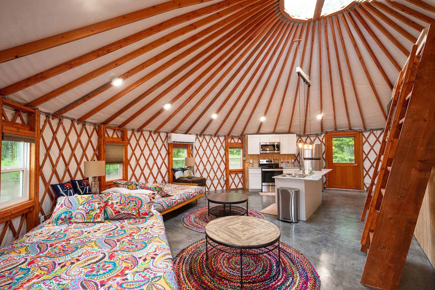 Open-concept yurt interior showing full kitchen and sleeping area under a lattice roof